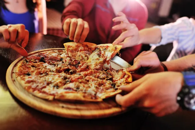 Händer som tar pizzabitar från träplatta